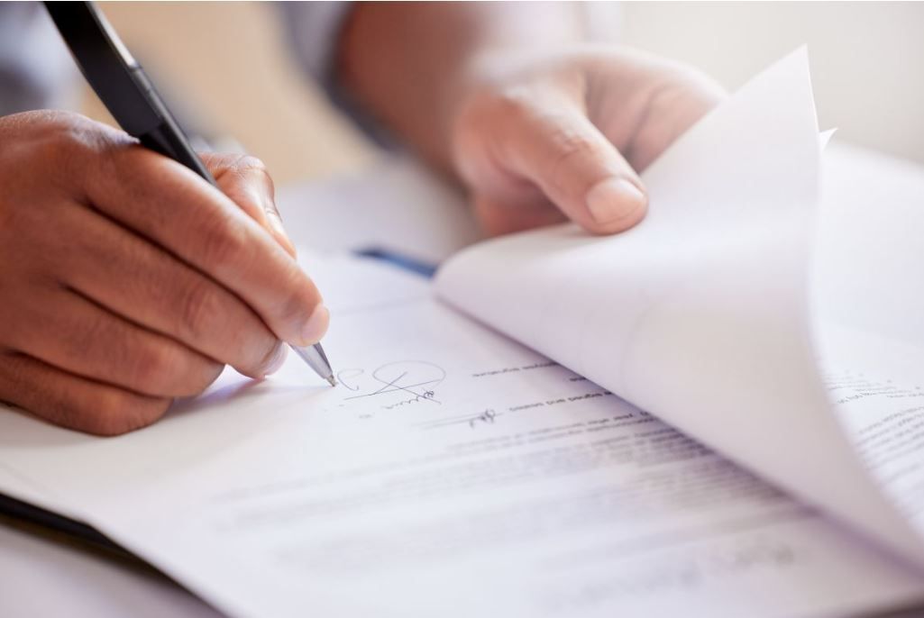 Close-up van een persoon die met een pen op een document schrijft en daarbij een pagina omslaat.