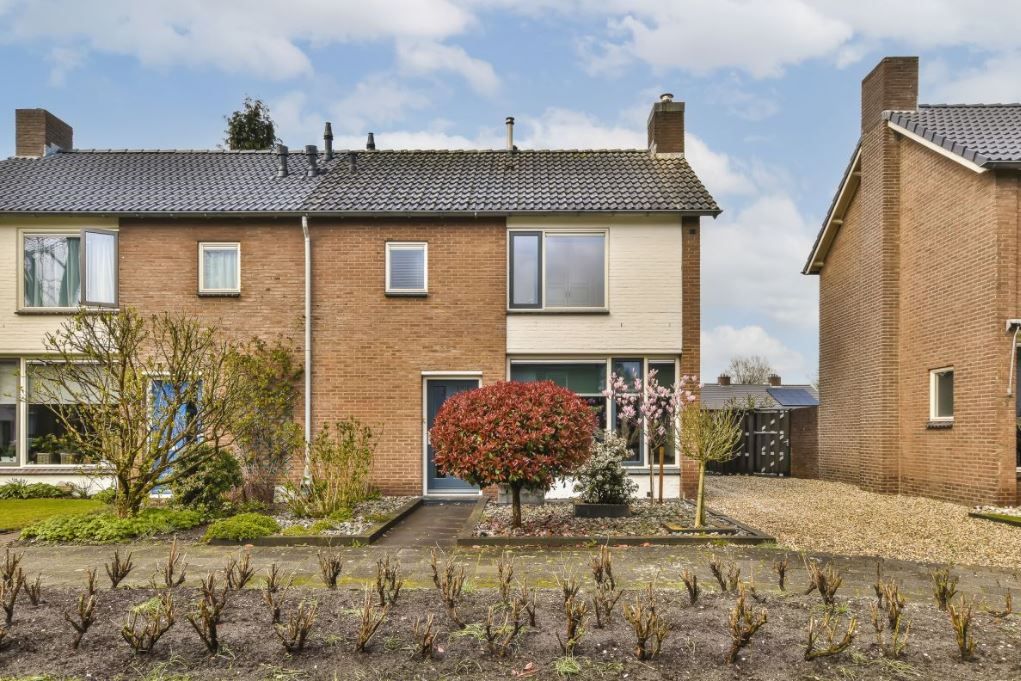 Een twee verdiepingen tellende, roodbruine bakstenen halfvrijstaande woning met een zadeldak, een voortuin en een oprit met grind.