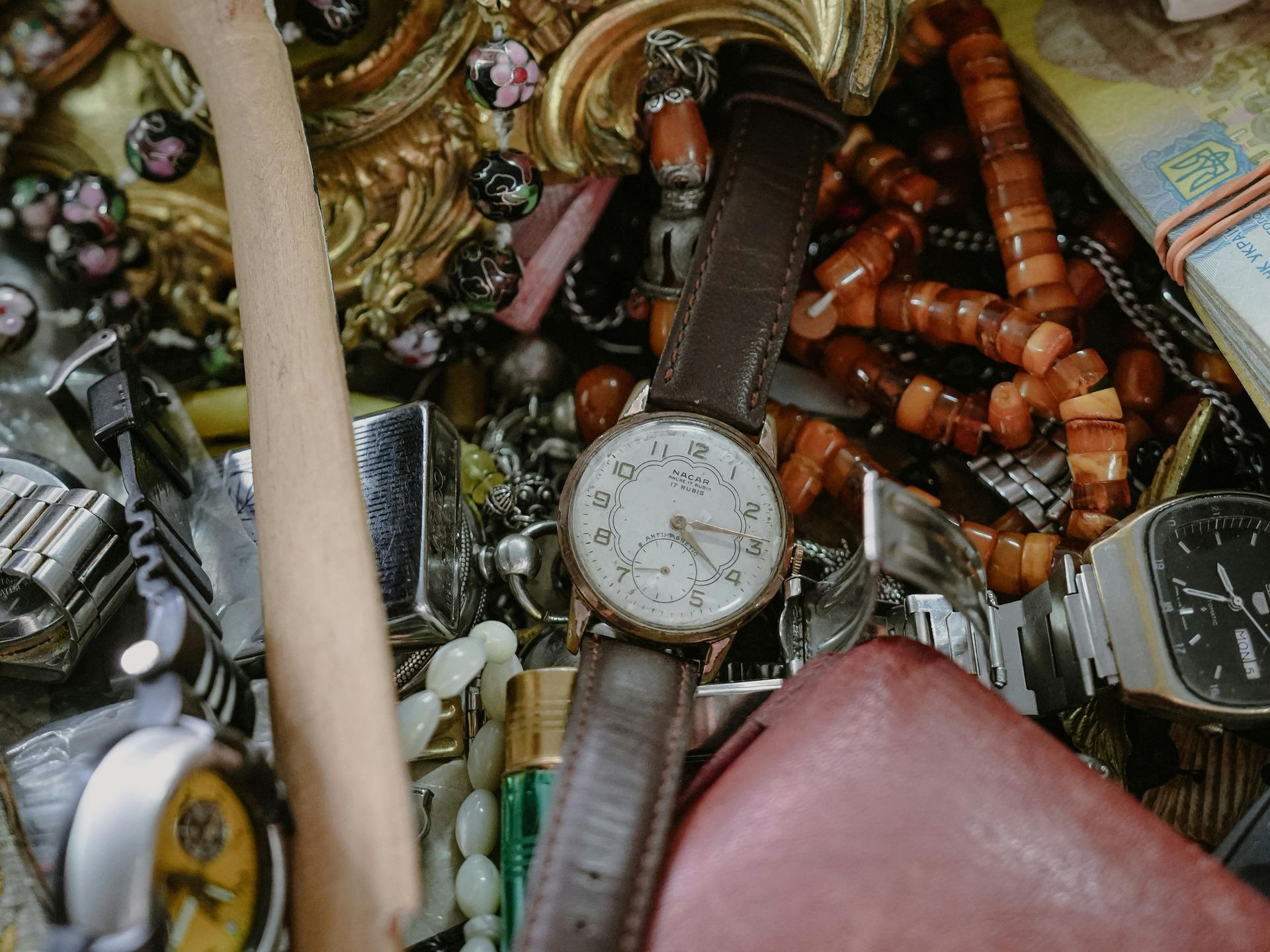 Een close-up van een rommelige verzameling horloges, kralen, sierlijk metaalwerk en een lichtbruin houten voorwerp.