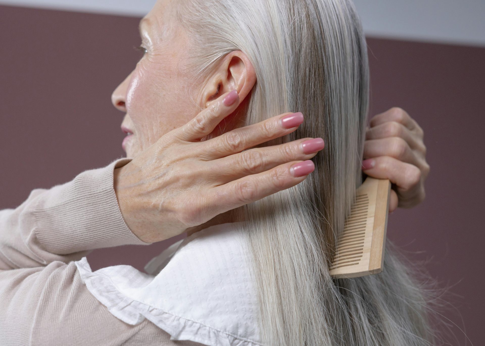 Iemand met lang, grijs wordend haar gebruikt een houten kam om zijn of haar haar te stylen.