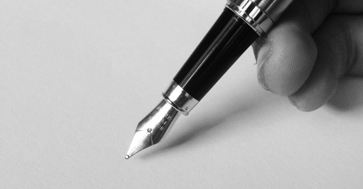Een hand houdt een vulpen vast, klaar om te schrijven op een effen wit oppervlak.
