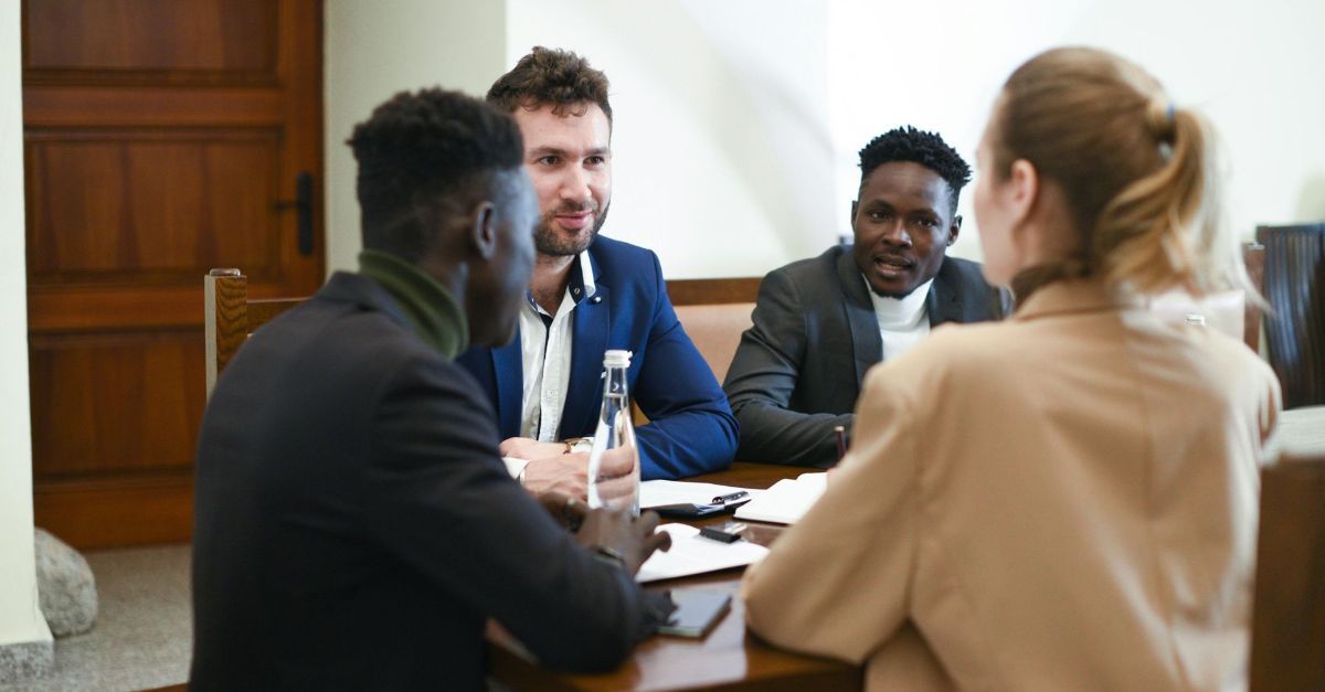 Vier collega's in zakelijke kleding zitten rond een tafel in een kantooromgeving en voeren een gezamenlijke discussie.