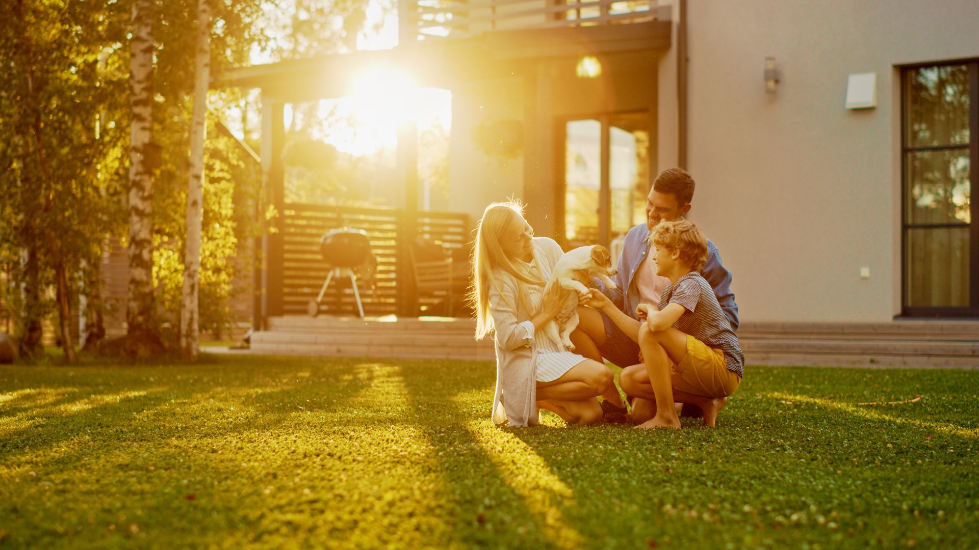 Family playing with a dog on a sunny lawn outside a house at sunset