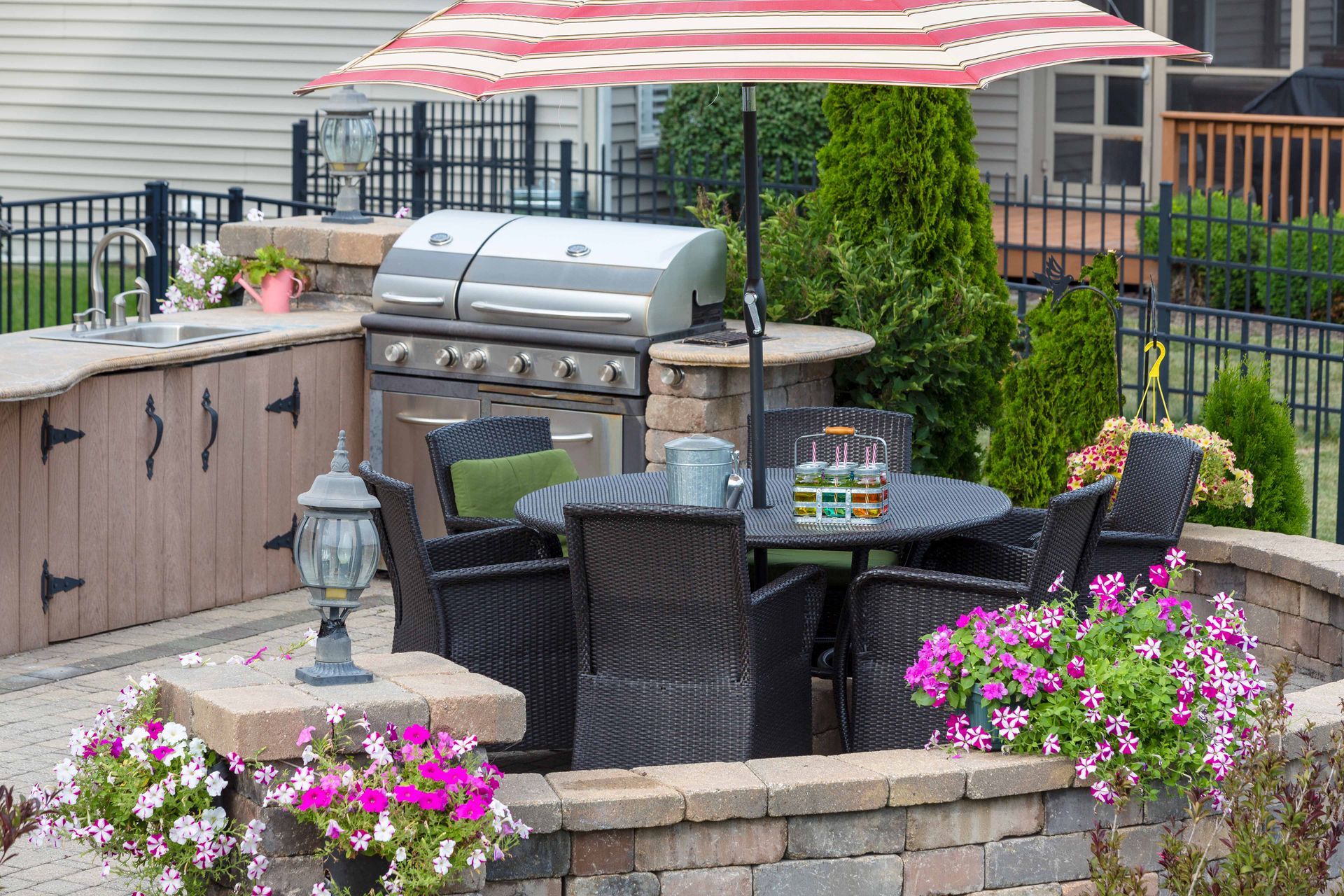 Outdoor patio with grill, dining table, umbrella, and surrounding brick wall with flowers.