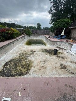 Empty drained swimming pool with cracked tile deck and cloudy sky, viewed from the shallow end