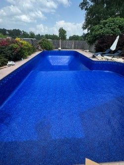Empty blue-lined backyard swimming pool with surrounding garden and lounge chairs