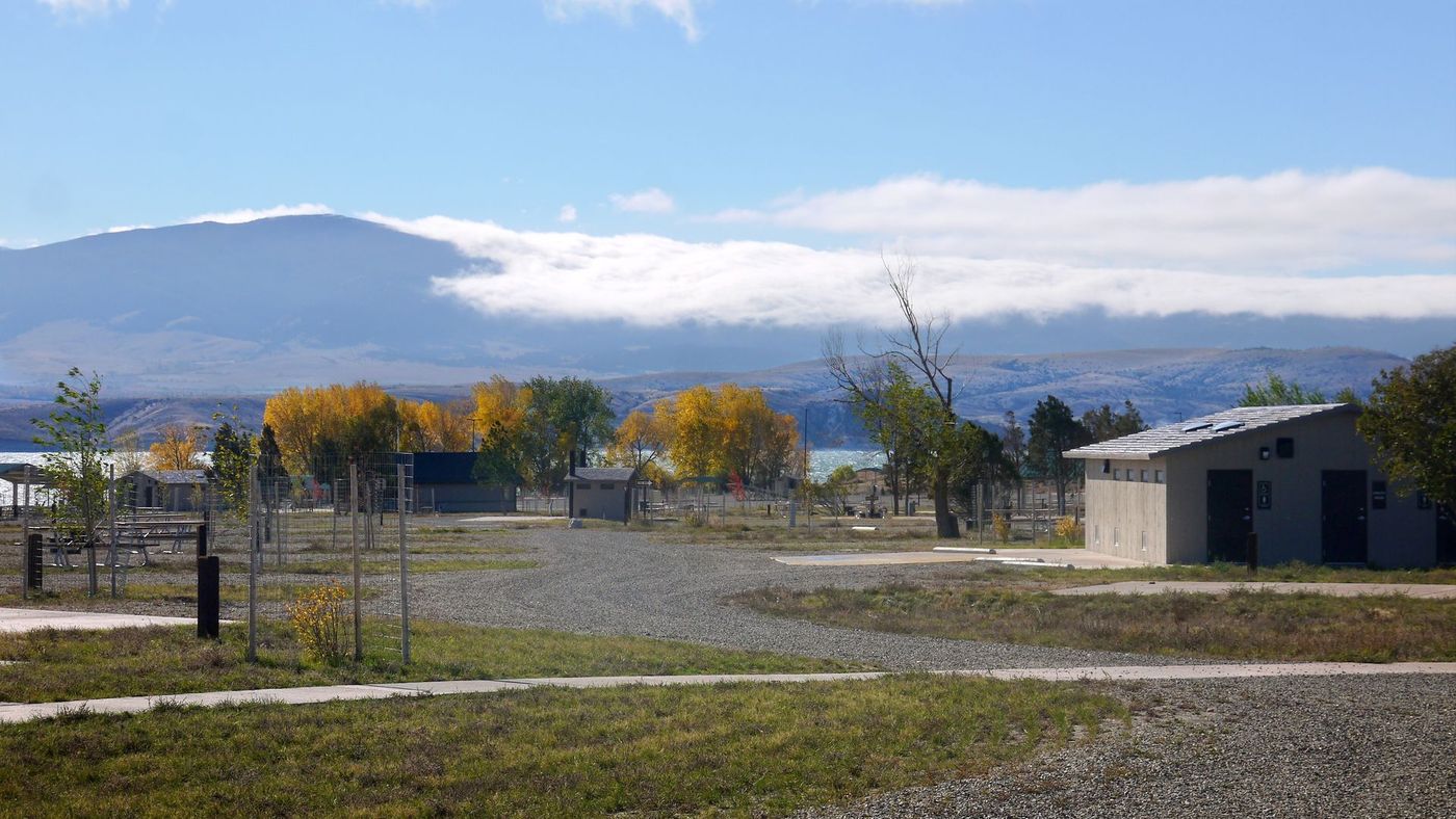 Open field with scattered trees, a small building, and mountains under a partly cloudy sky