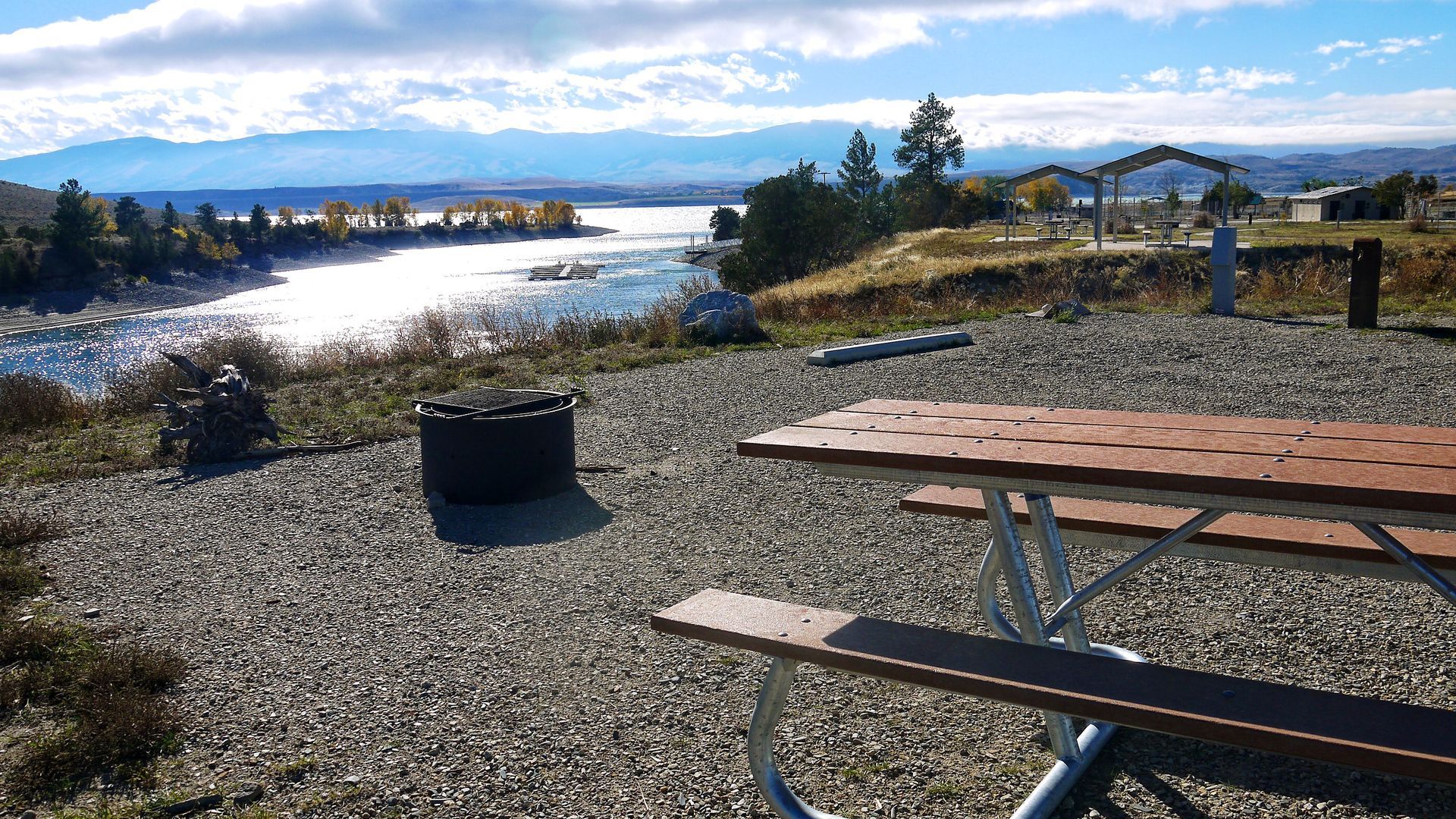 Picnic table and fire ring overlooking a river under a bright blue sky