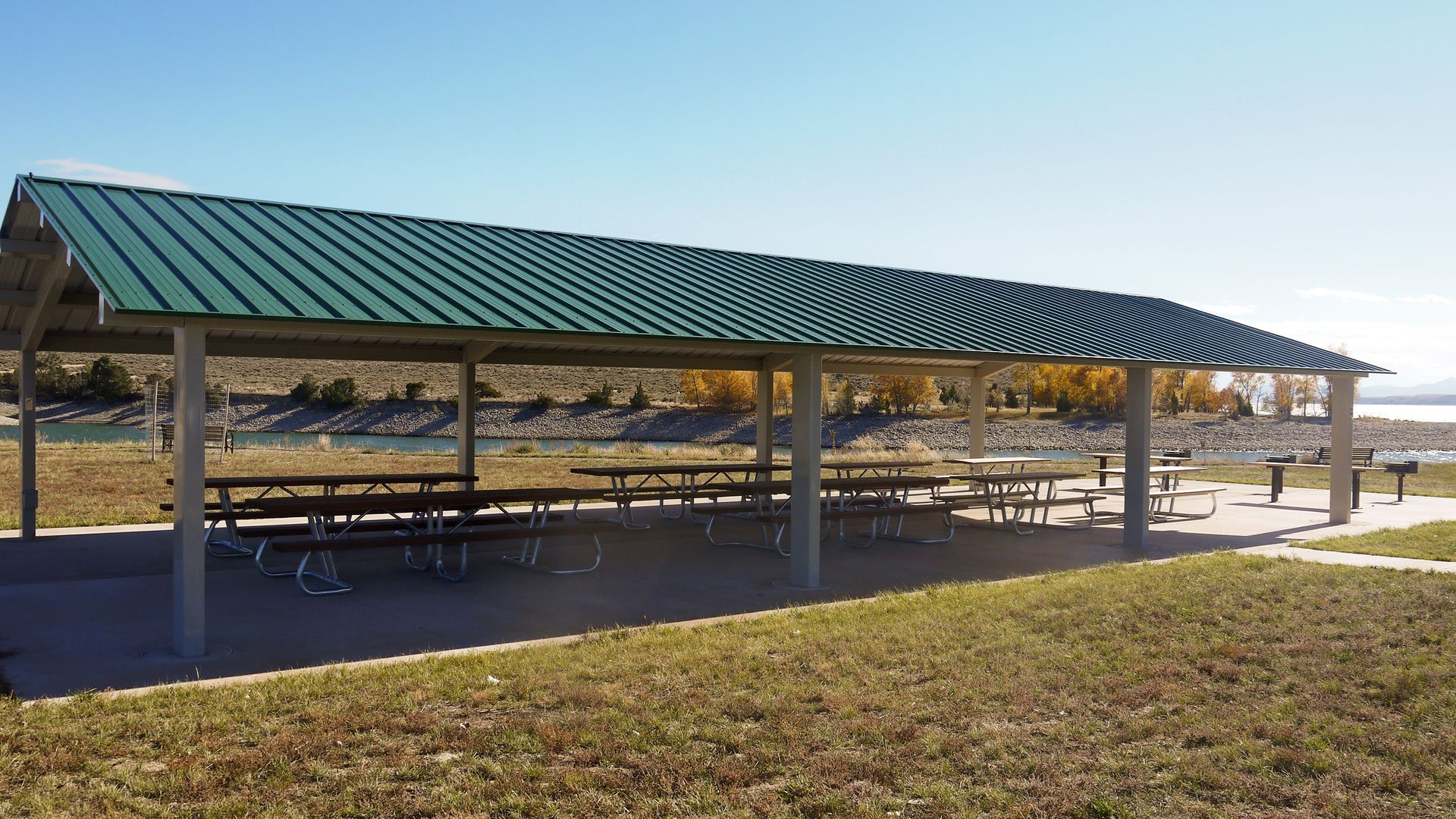 Open picnic shelter with green metal roof and benches in a grassy park area
