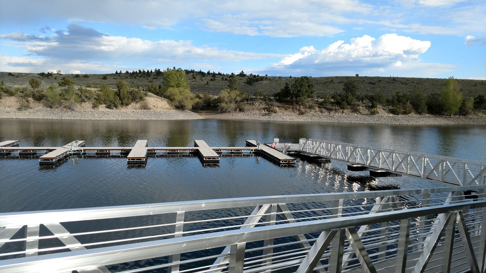 Marina with floating docks on calm water, viewed from a metal bridge under a partly cloudy sky