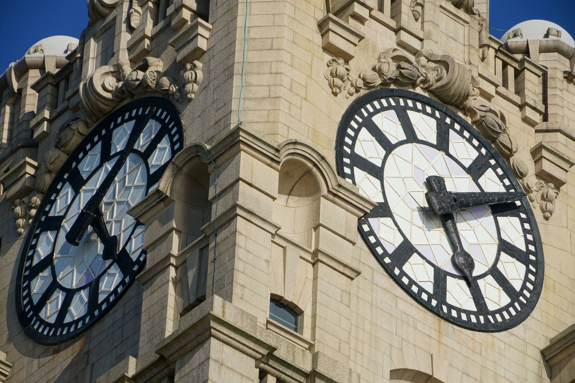 Two large clock faces on a stone tower against a blue sky