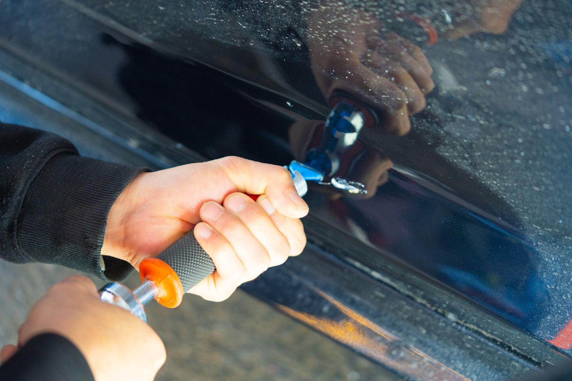 Close-up of hands using a dent puller tool to repair a car door surface. Close-up of hands using a dent puller tool to repair a car door surface.