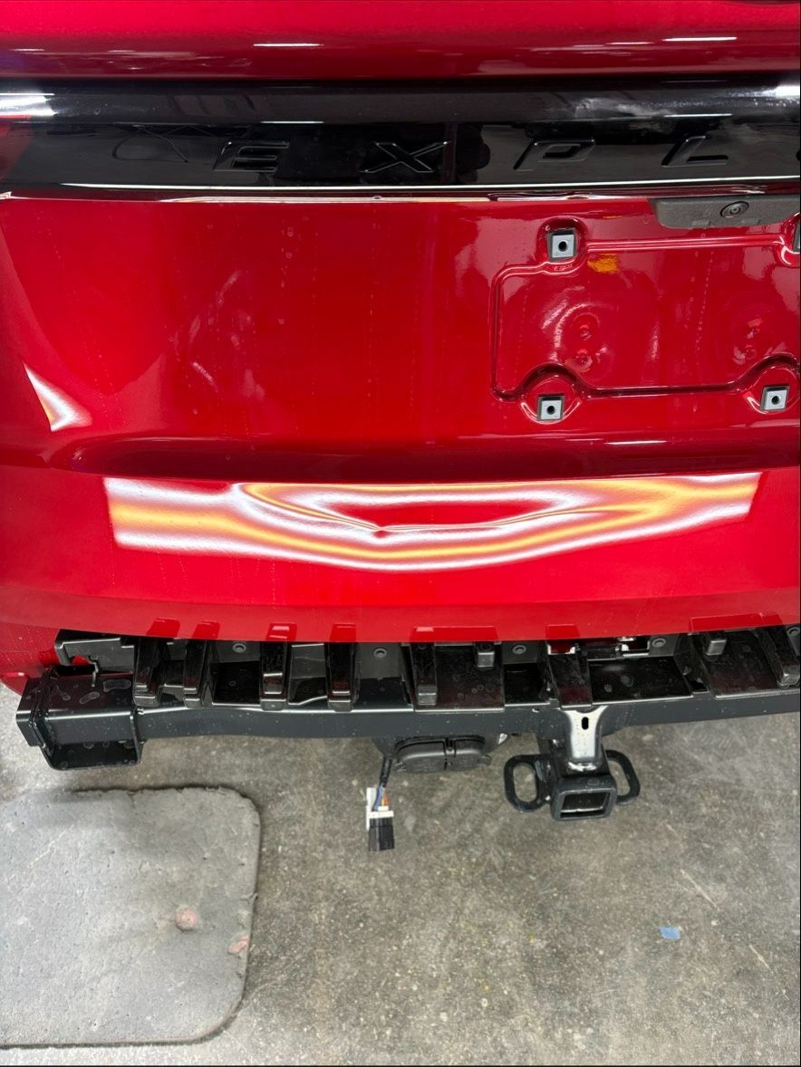 Close-up of a red car’s rear bumper with a tow hitch in a garage.