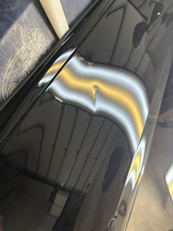Close-up of a glossy black car door with a bright yellow and white reflection curve.