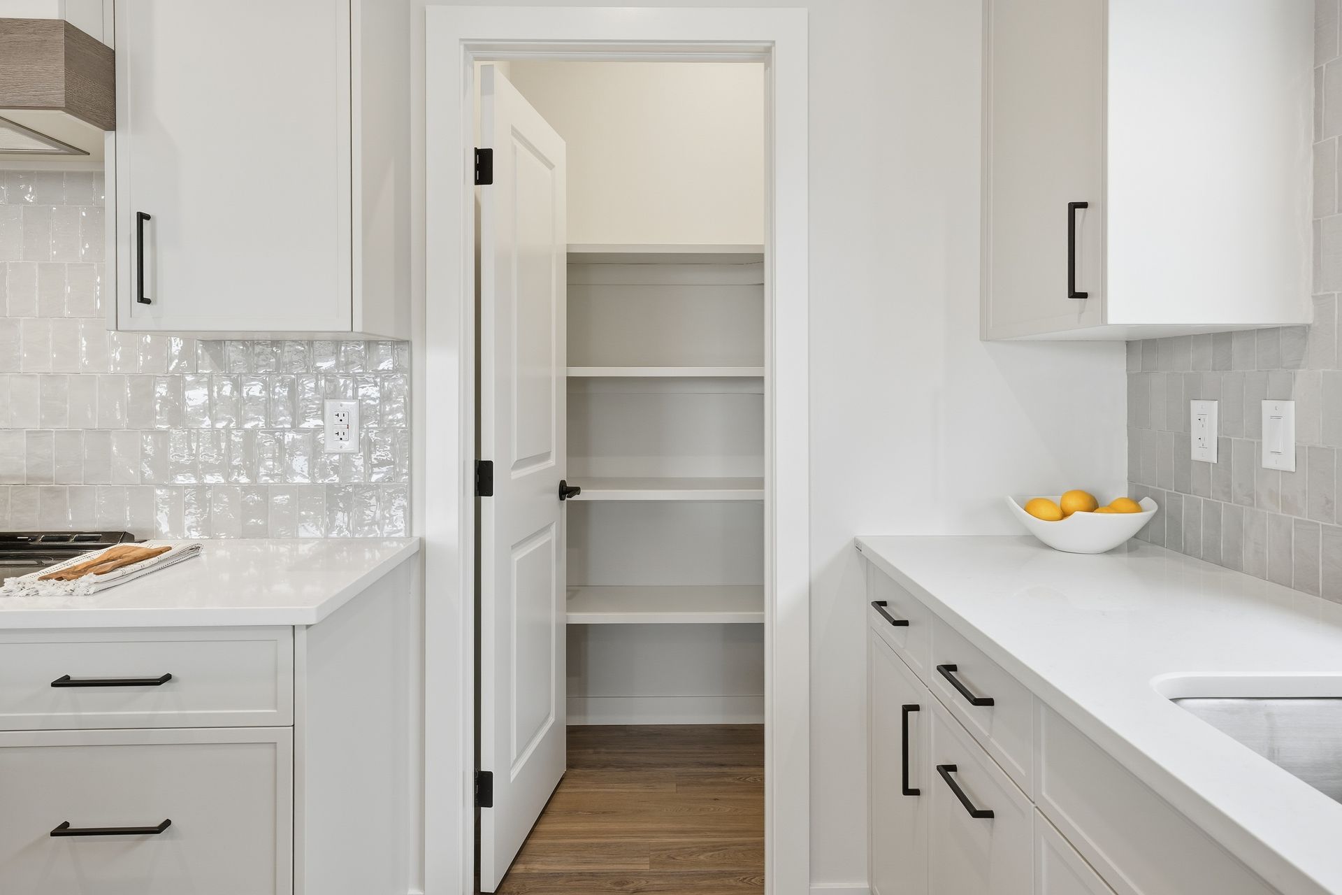 A white modern kitchen featuring white cabinets, a walk-in pantry with shelves, and light gray tiled backsplashes. A white modern kitchen featuring white cabinets, a walk-in pantry with shelves, and light gray tiled backsplashes.