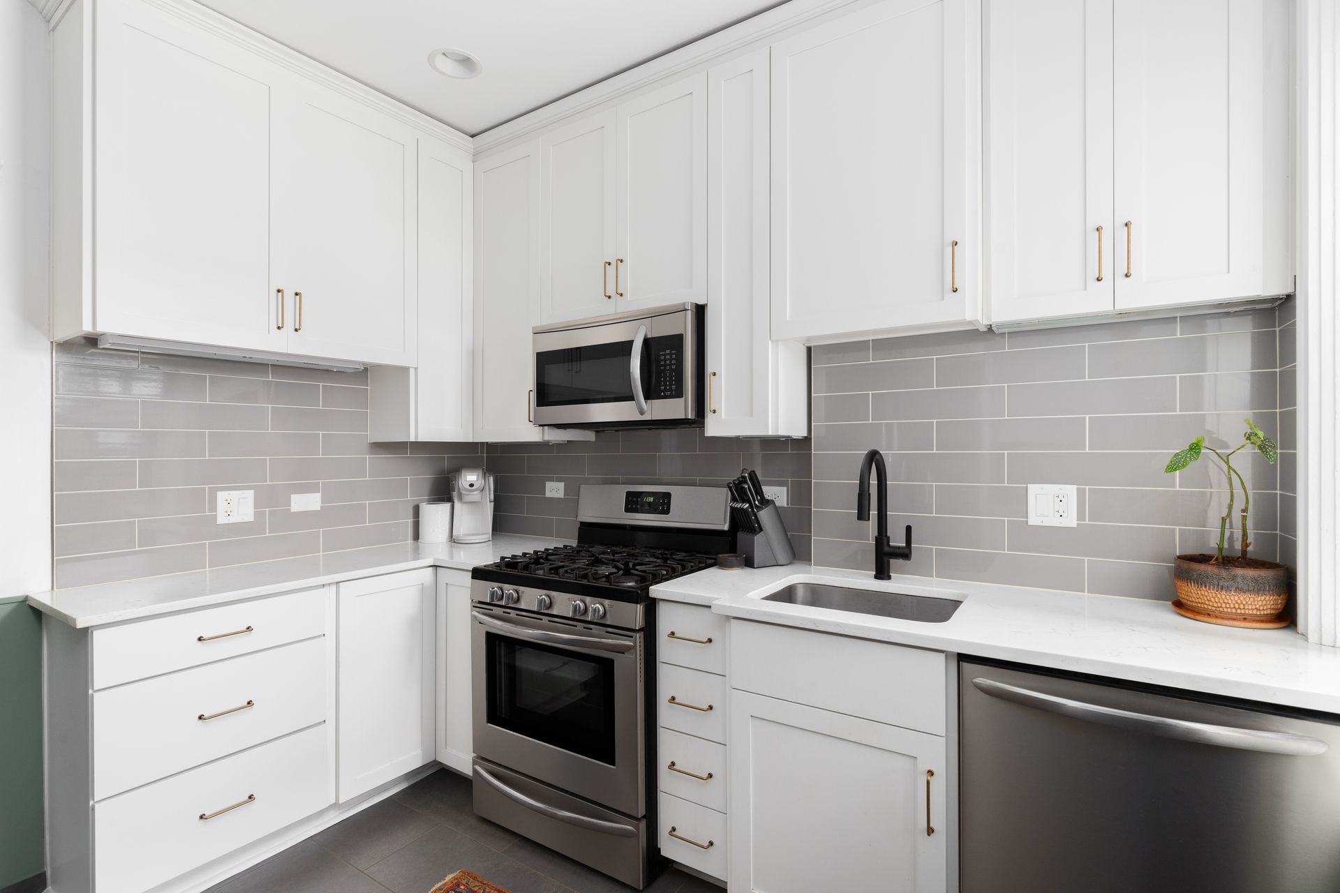A clean, modern kitchen with white cabinets, stainless steel appliances, grey subway tile backsplash, and white counters.