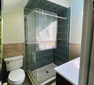 A bathroom vanity with a grey cabinet and stone countertop, next to white wainscoting and a door leading to a room.