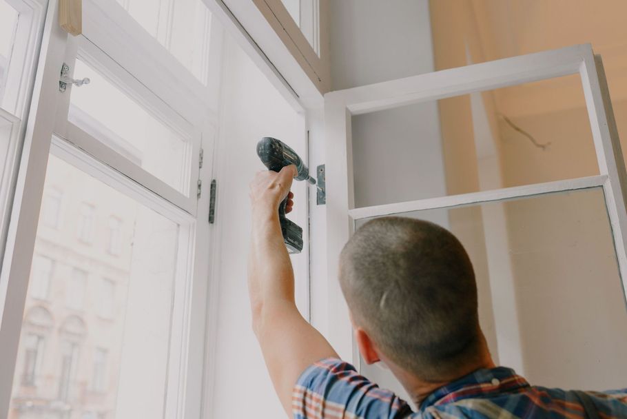 Person using a drill to install a white window frame indoors