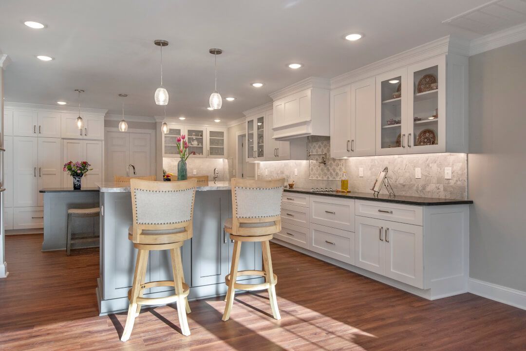 Home Additions: A kitchen with white cabinets, wooden floors, stools, and a large island.