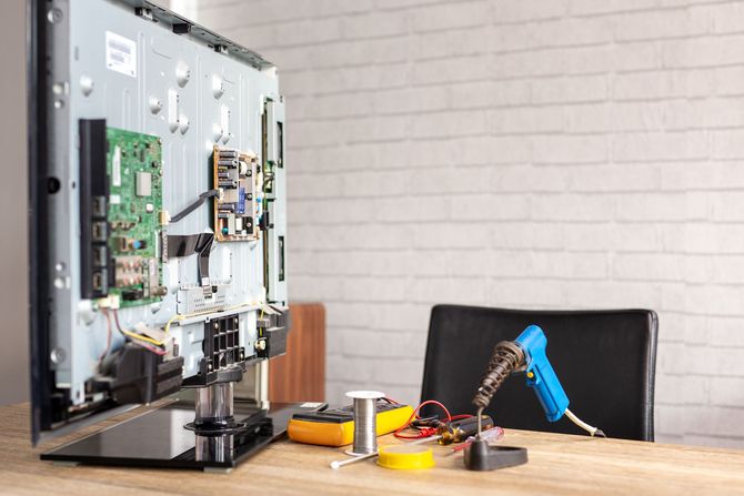 TV being repaired, back open, with repair tools on a table.