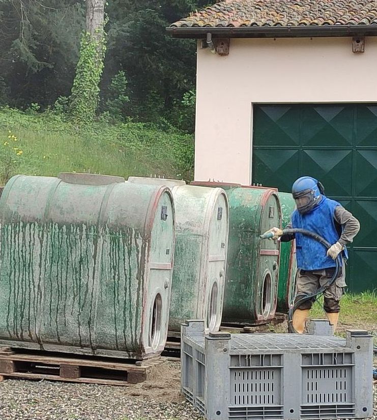 Persona che esegue la sabbiatura di serbatoi industriali verdi all'esterno di un edificio.