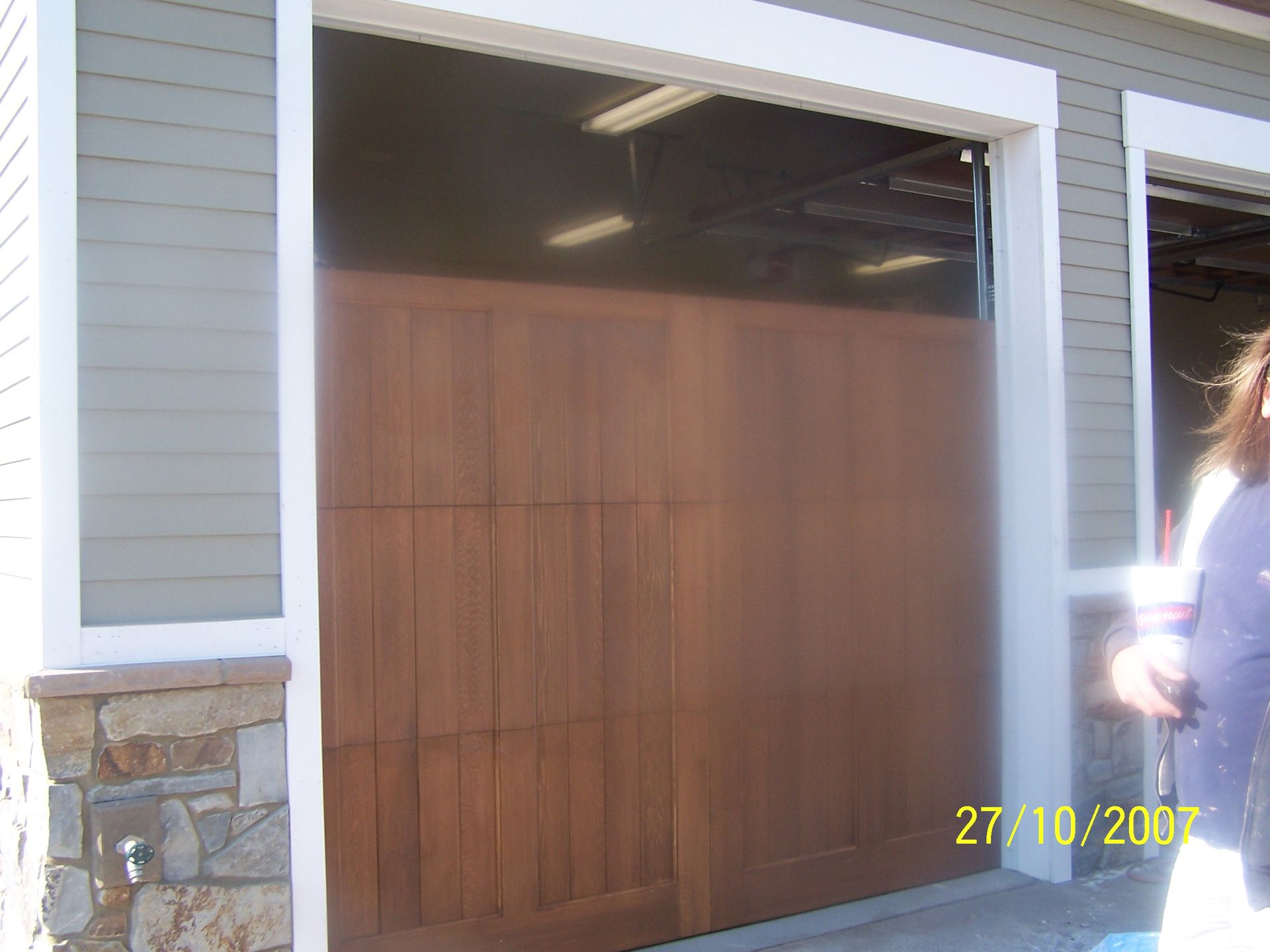 A woman is standing in front of a wooden garage door on 27/10/2007