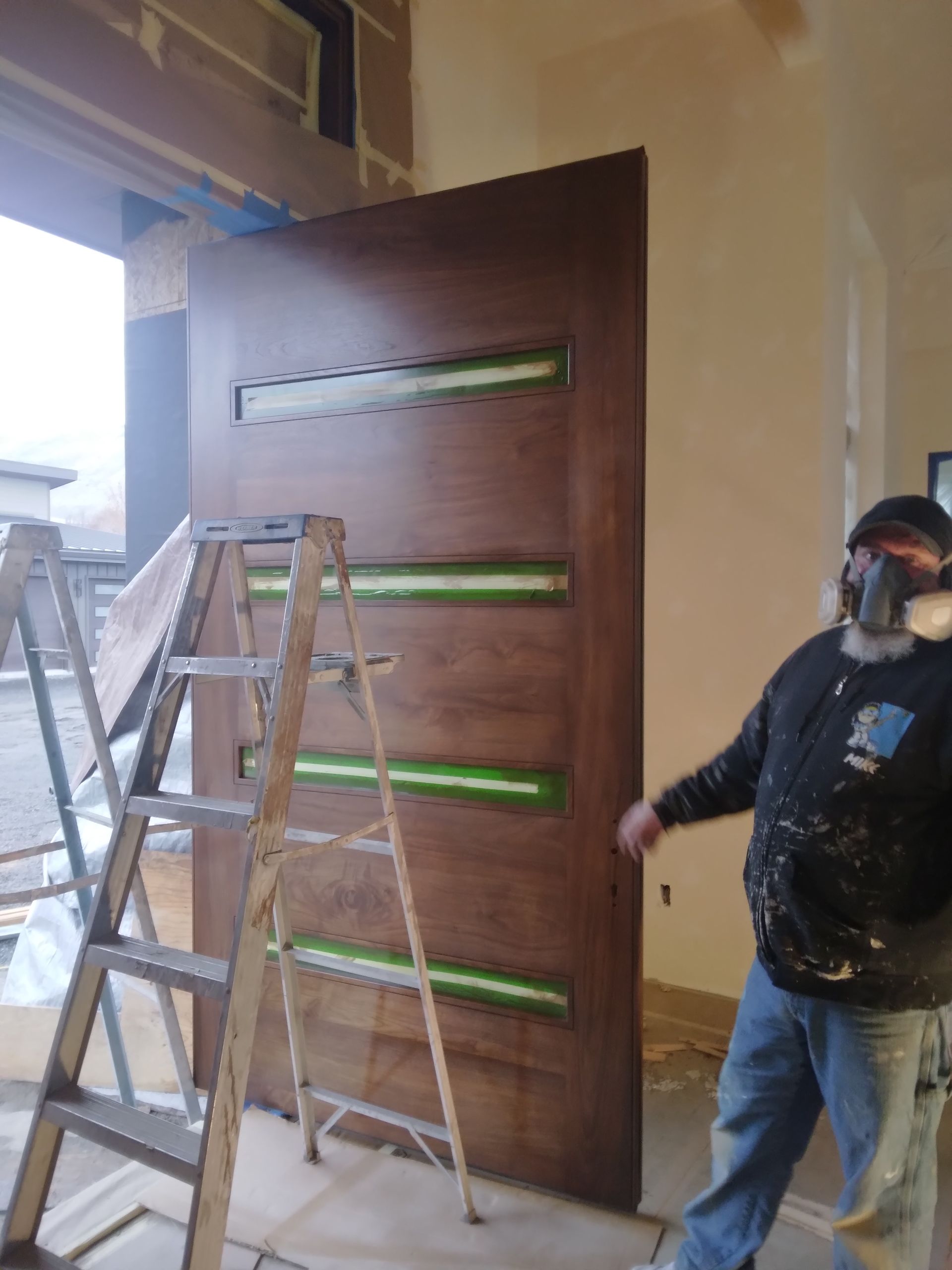 A man wearing a mask is standing next to a ladder in front of a wooden door.