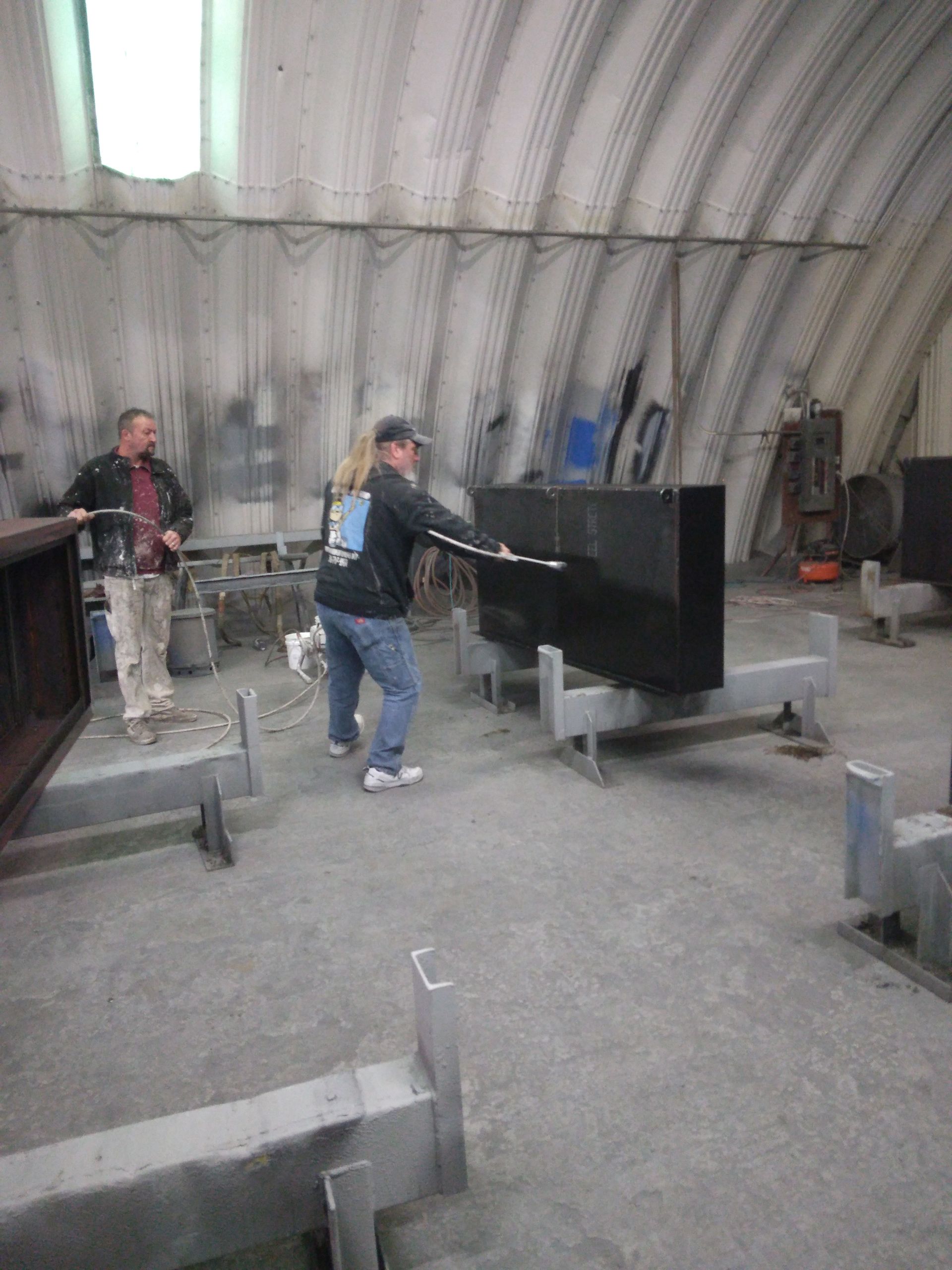A man and a woman are working on a piece of metal in a factory.