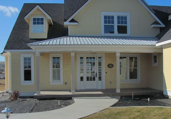 A yellow house with a porch and a gray roof