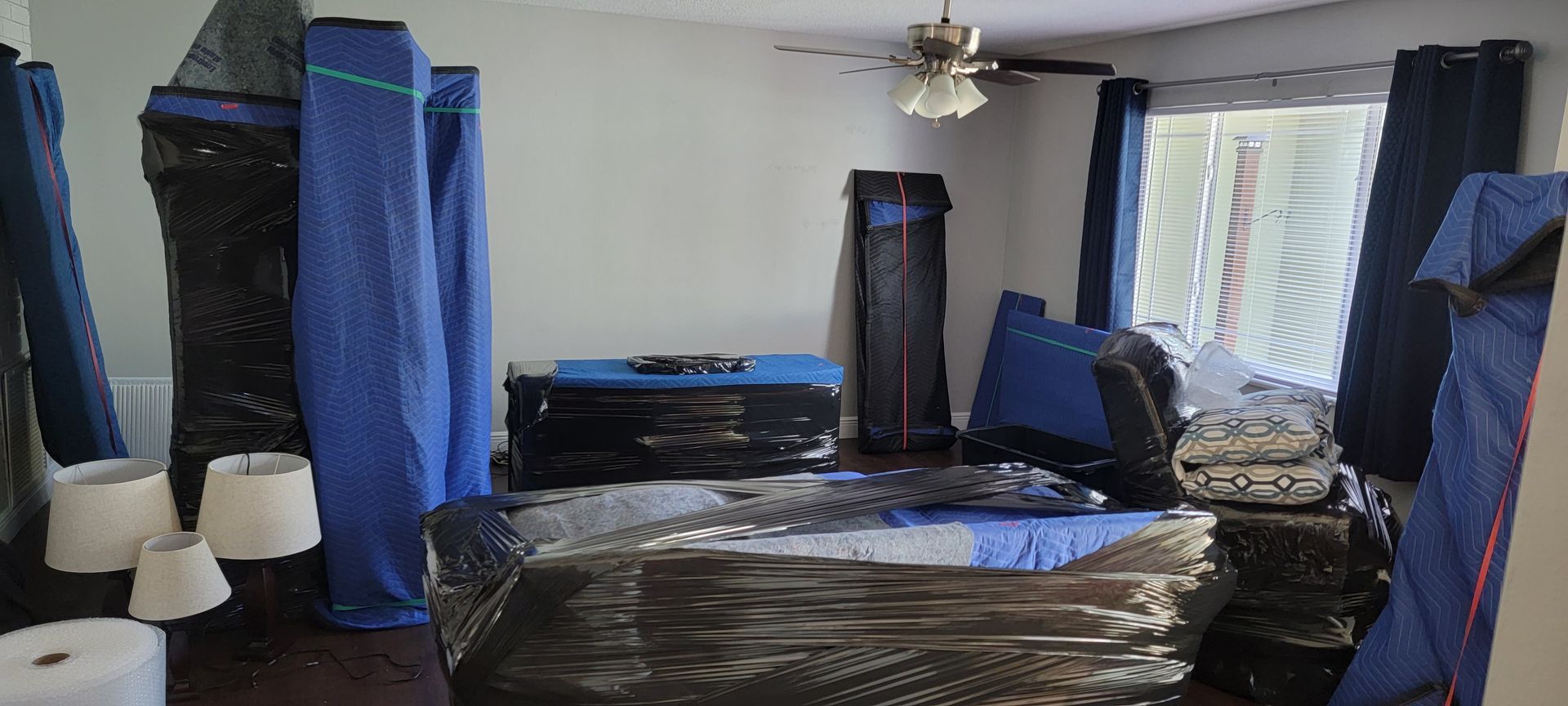 Living room with furniture covered in blue plastic, suggesting painting or renovation work