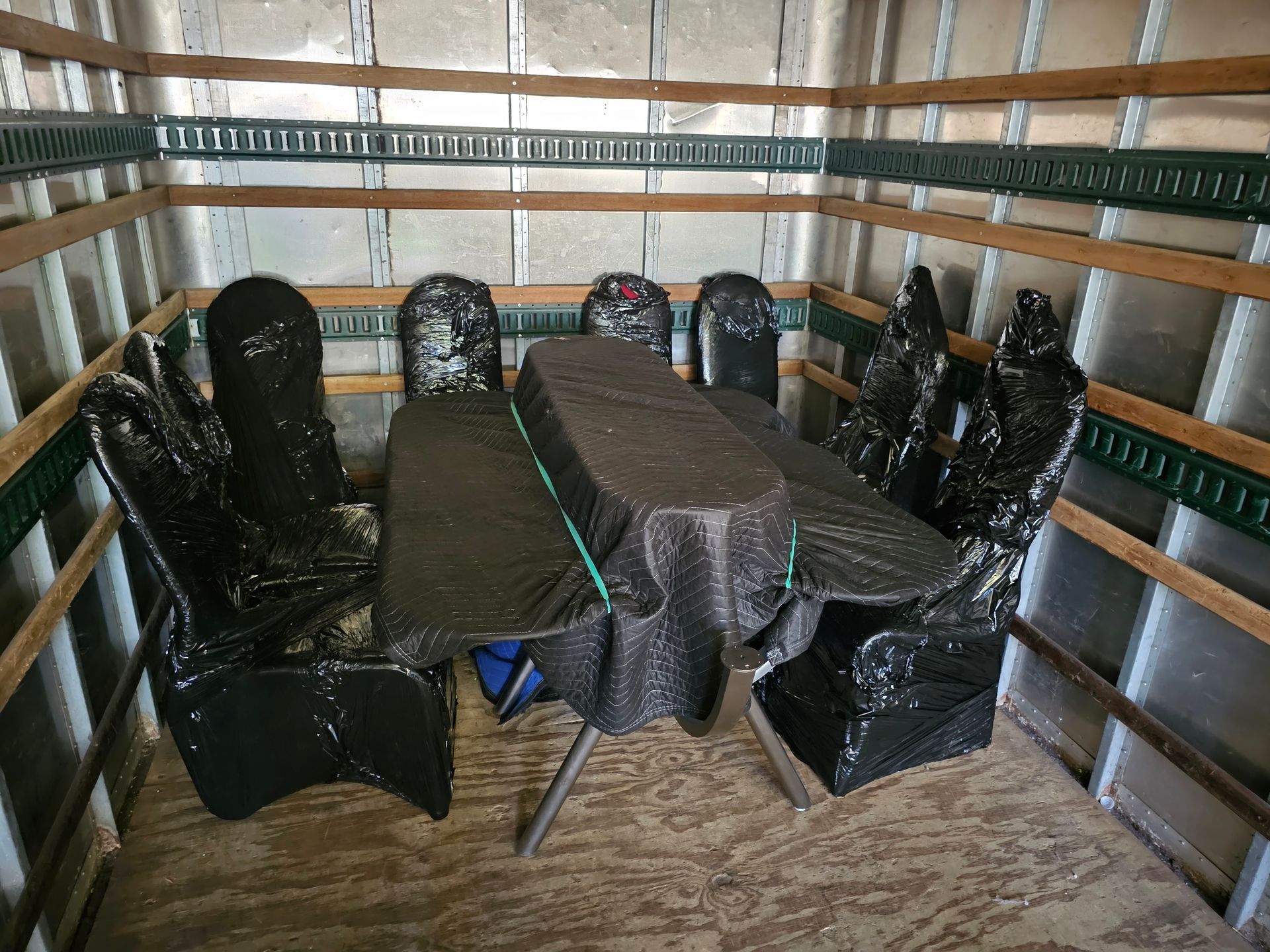 Covered table and chairs arranged inside the back of a moving truck