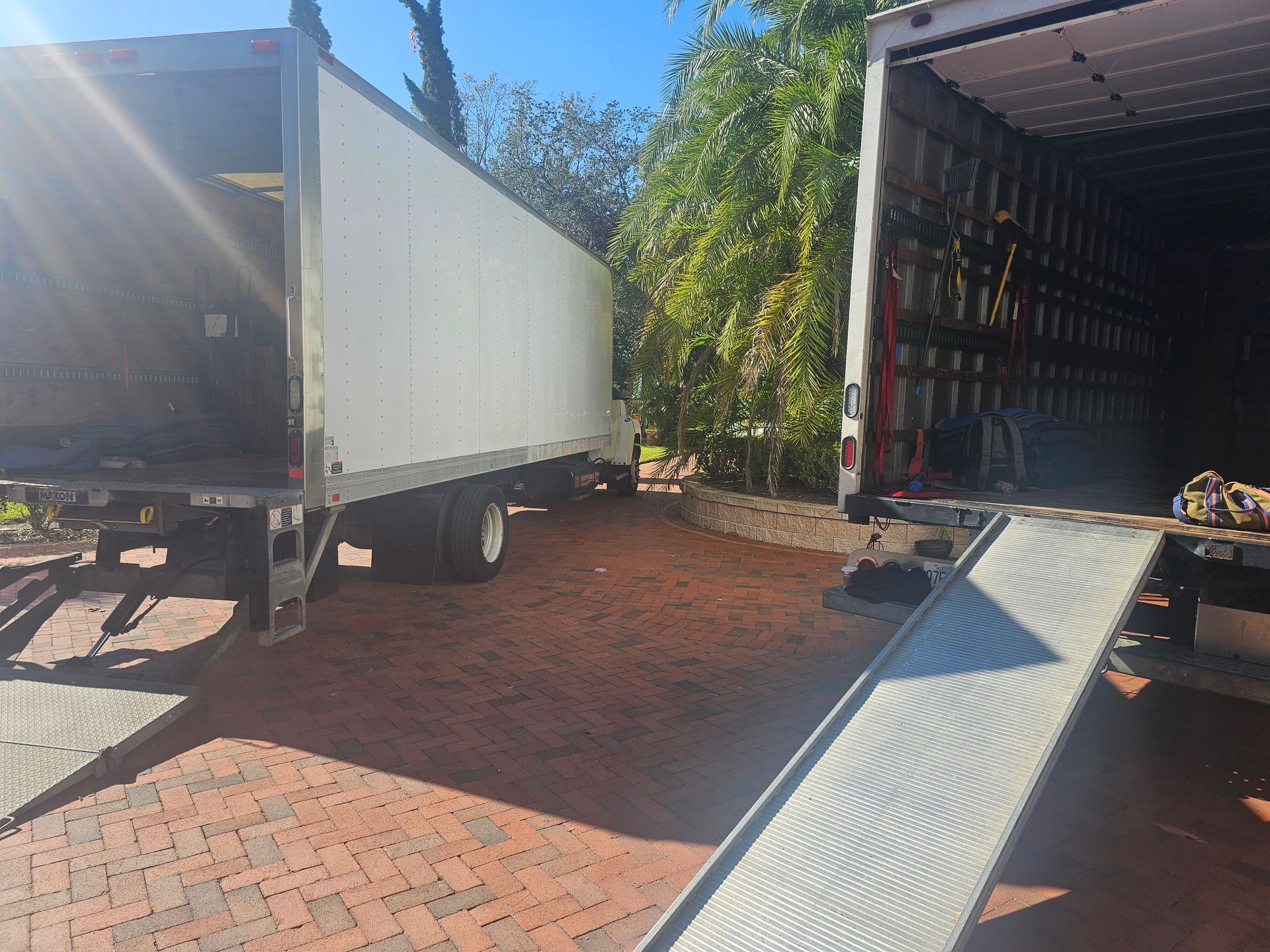 Open truck containers and a metal loading ramp on a brick driveway in bright sunlight