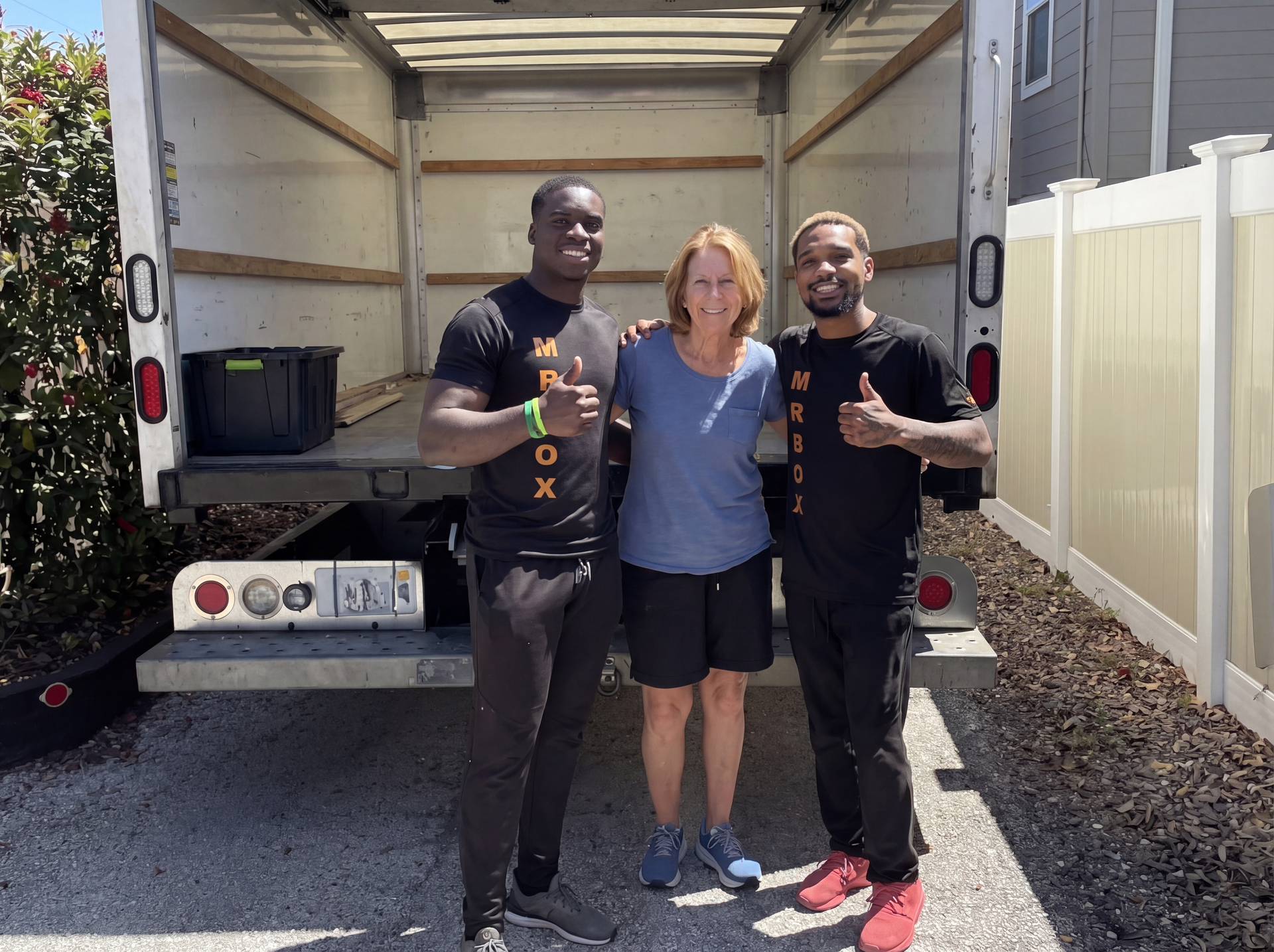 Three people standing in the back of a moving truck, smiling and posing outdoors.