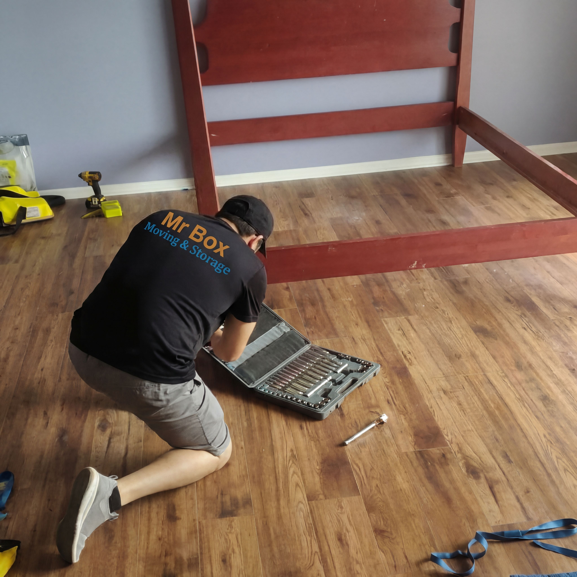 Person kneeling on wood floor, repairing an open tool case with scattered tools nearby.