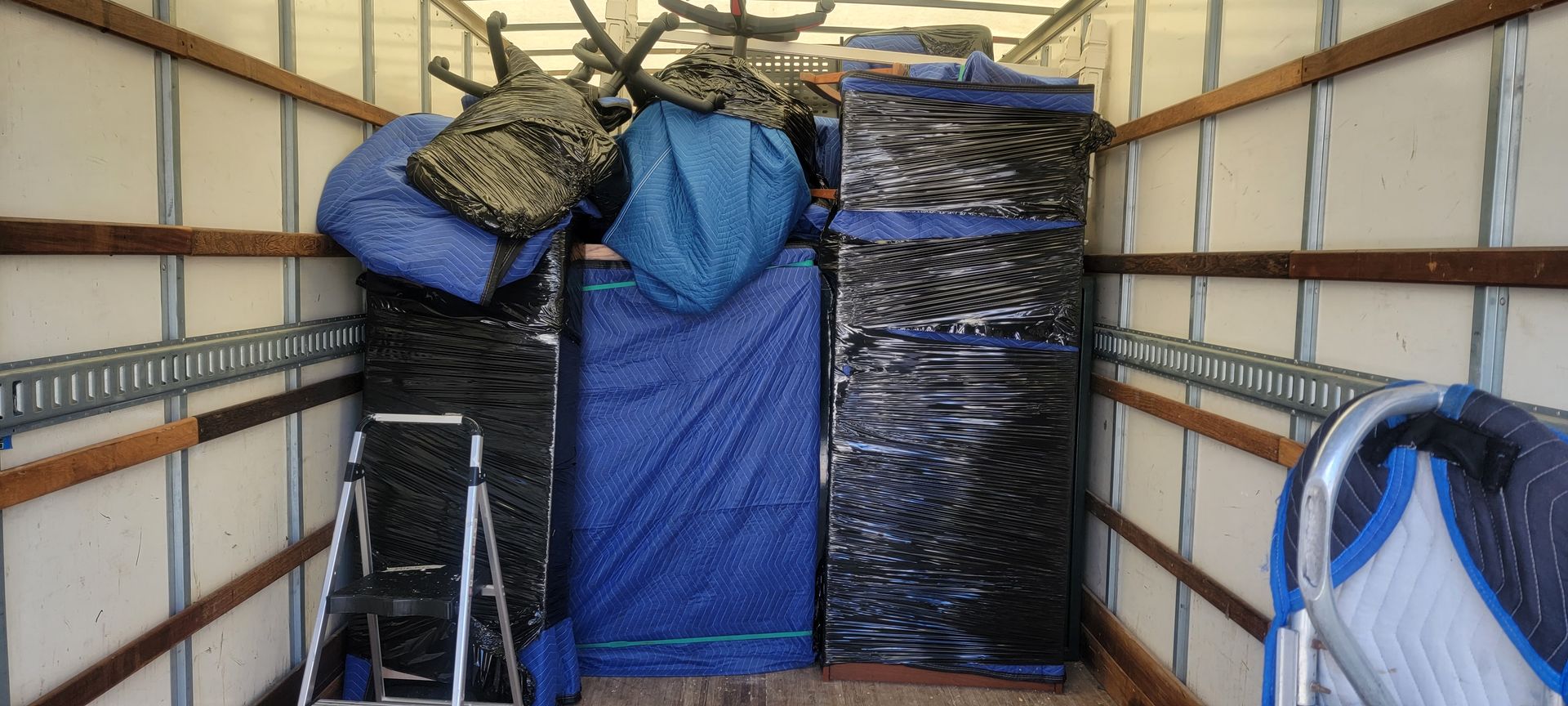 Packed moving truck with stacked bins, tarped furniture, and a folded ladder inside.