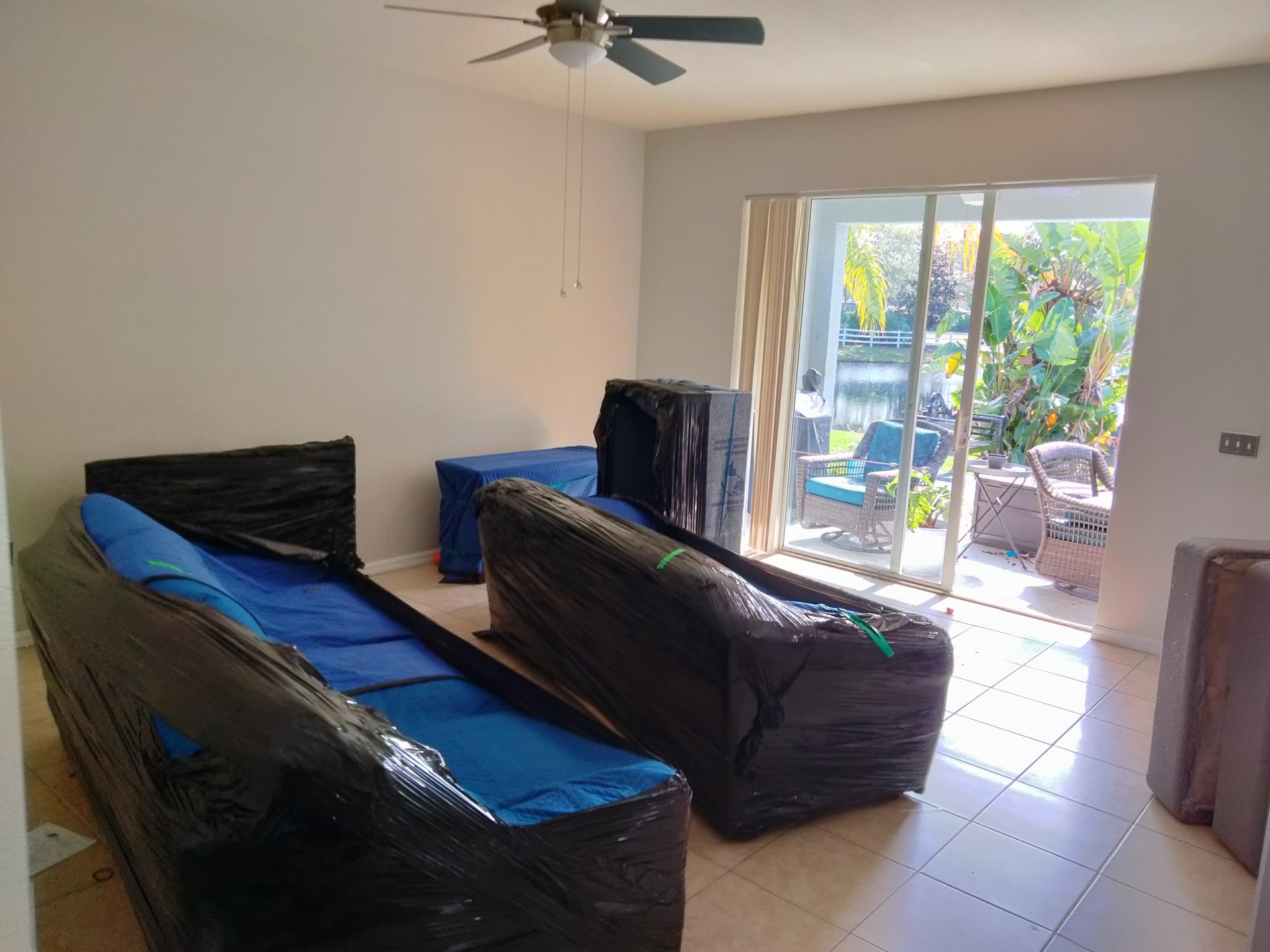 Living room with furniture covered in plastic, ceiling fan, and sliding doors to a sunny patio.