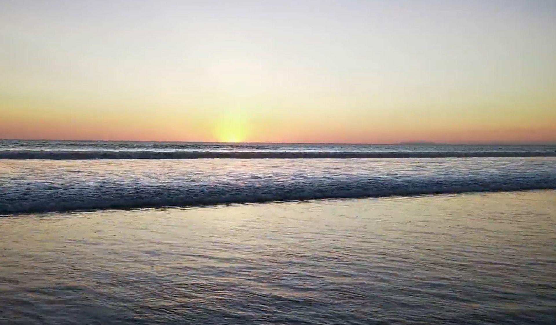 The sun is setting over the ocean and the waves are breaking on the beach.