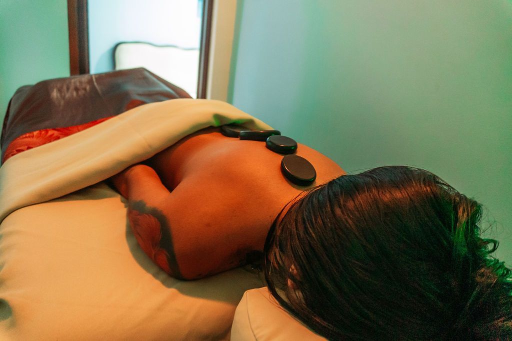 A woman is laying on a massage table with rocks on her back.