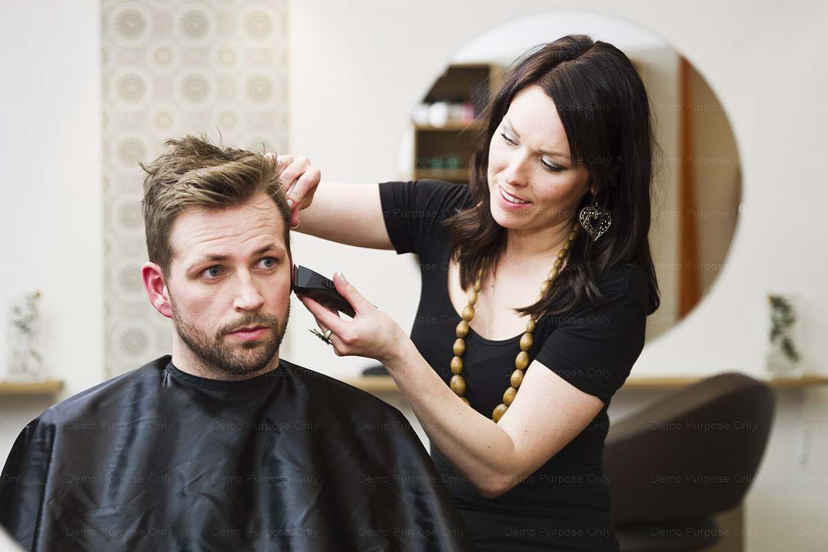A woman is cutting a man 's hair in a salon.