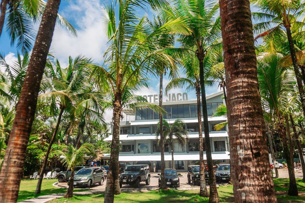 A hotel is surrounded by palm trees and cars parked in front of it.