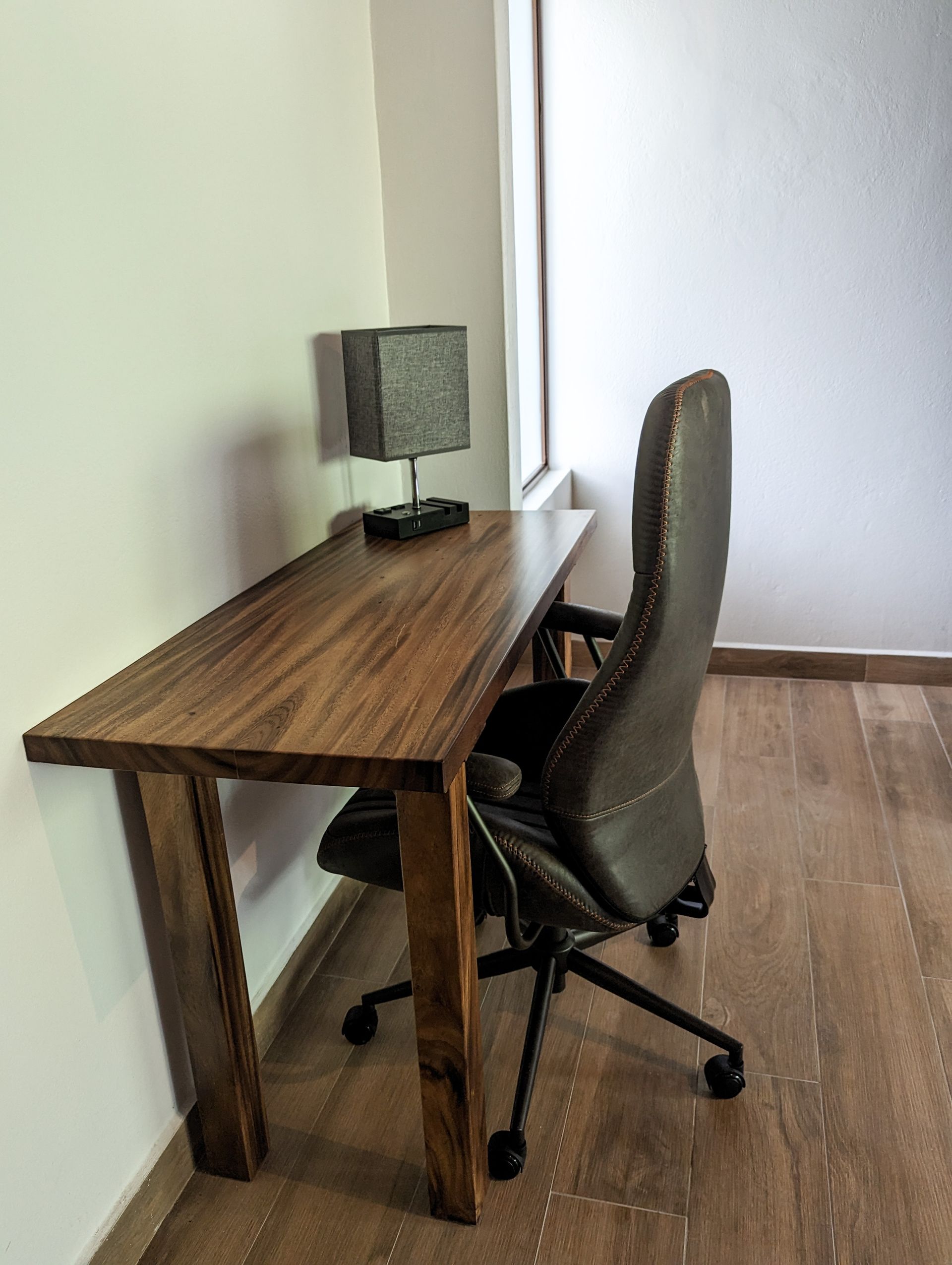A wooden desk with a chair and a lamp on it