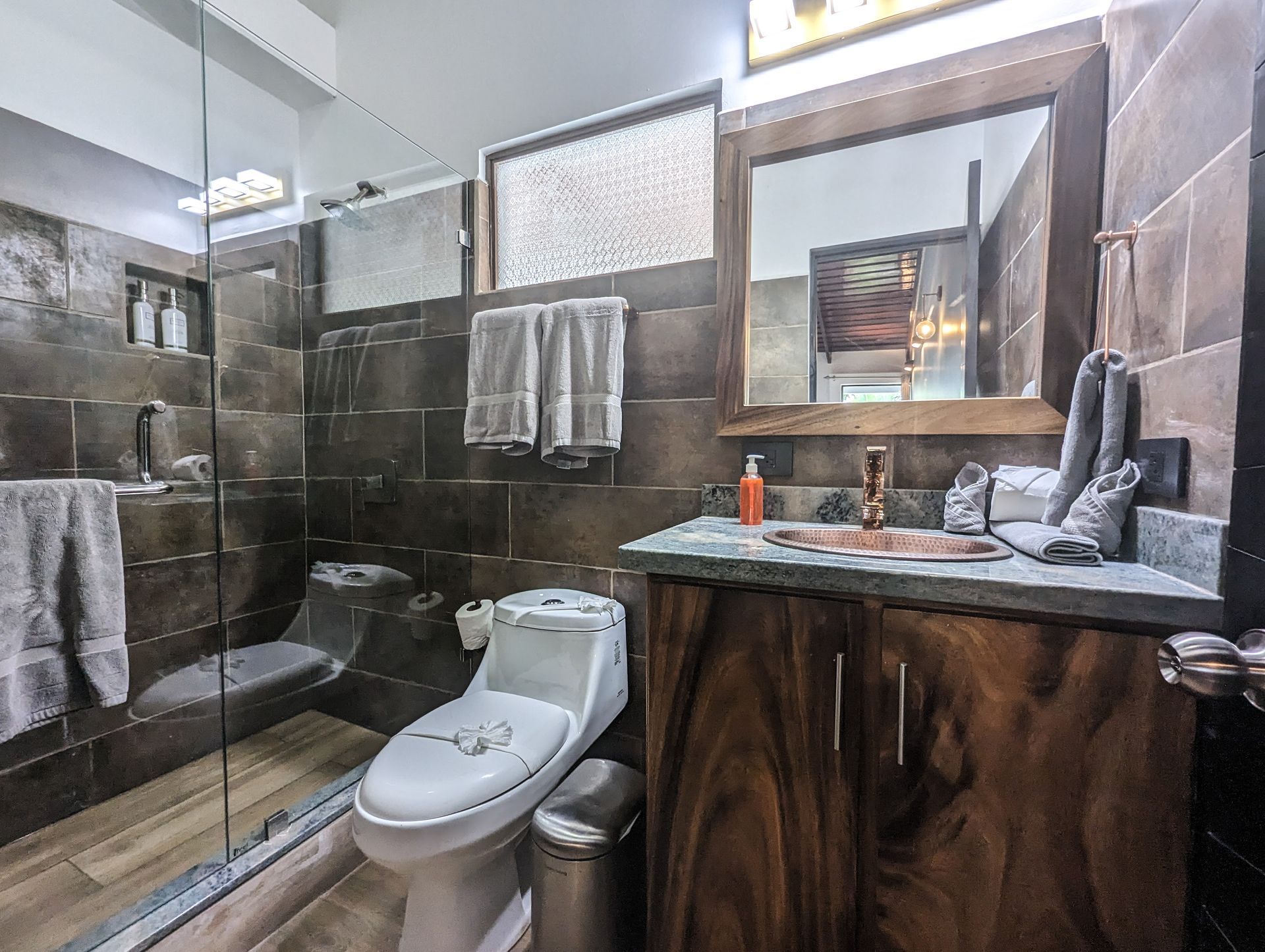 A bathroom with a toilet , sink , mirror and walk in shower.