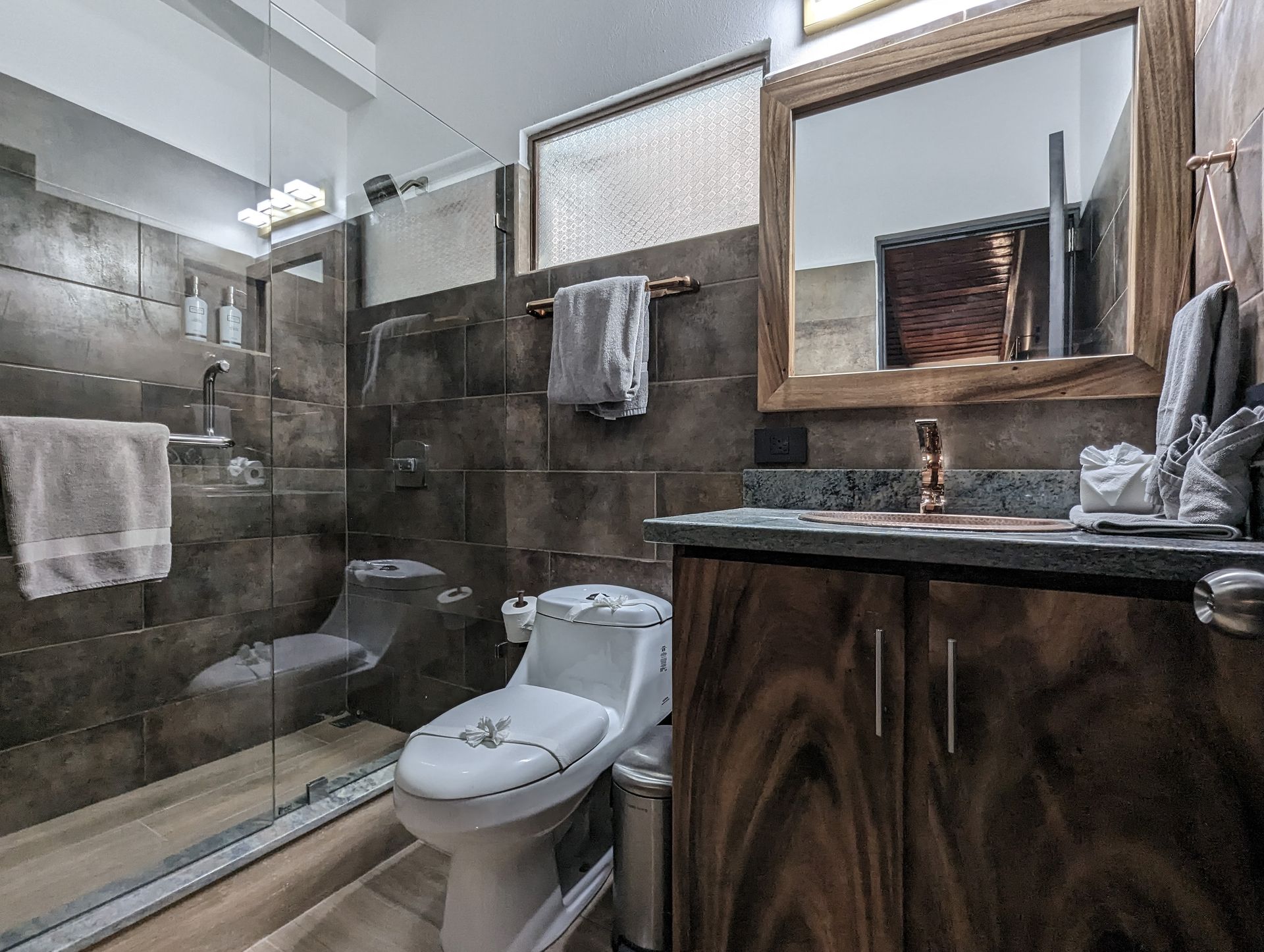 A bathroom with a toilet , sink , mirror and walk in shower.