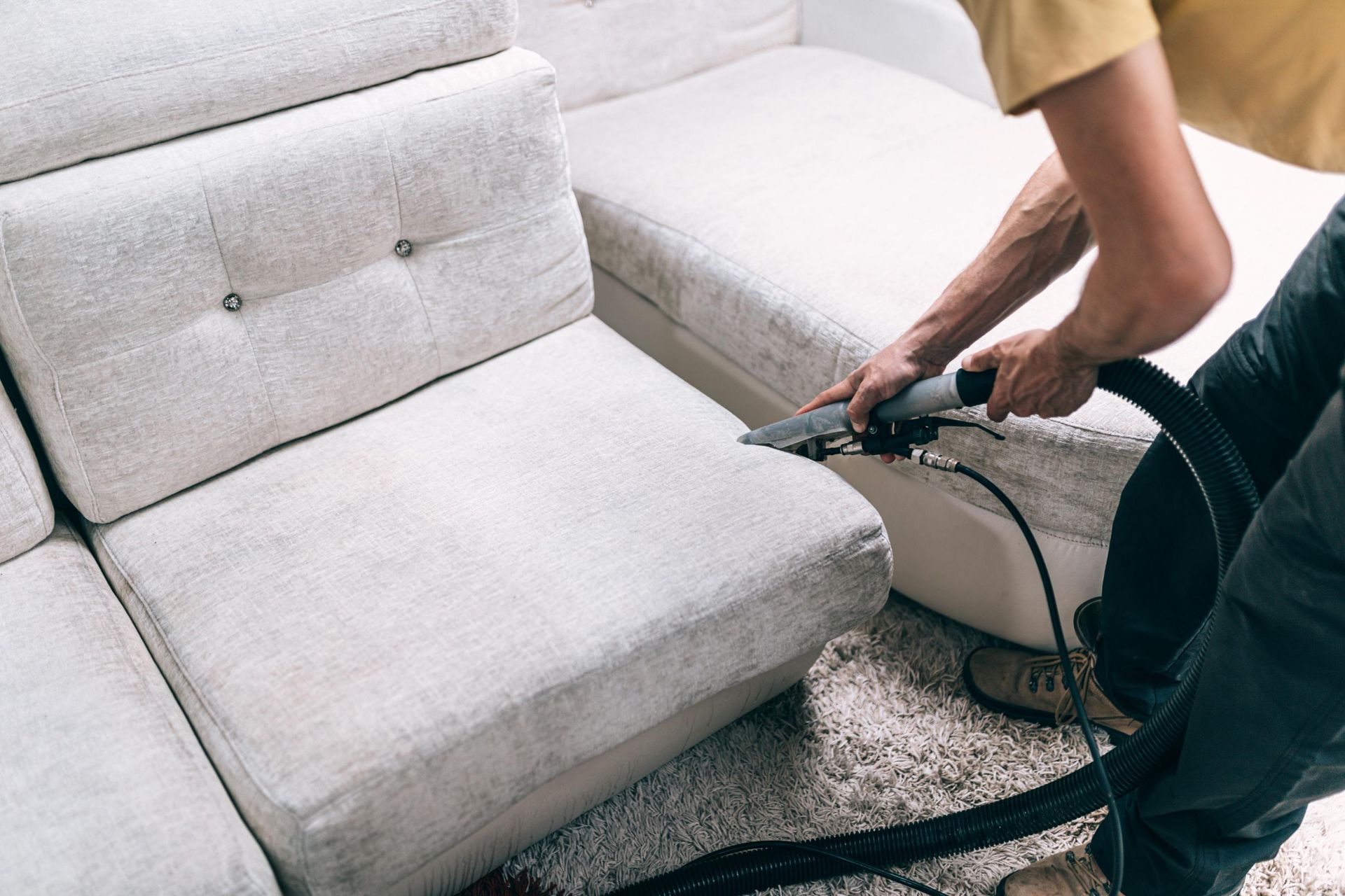 Person cleaning a white sectional sofa with an upholstery cleaner, indoors.