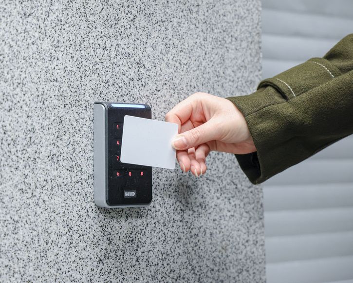 Hand holding a white access card near a wall-mounted card reader panel