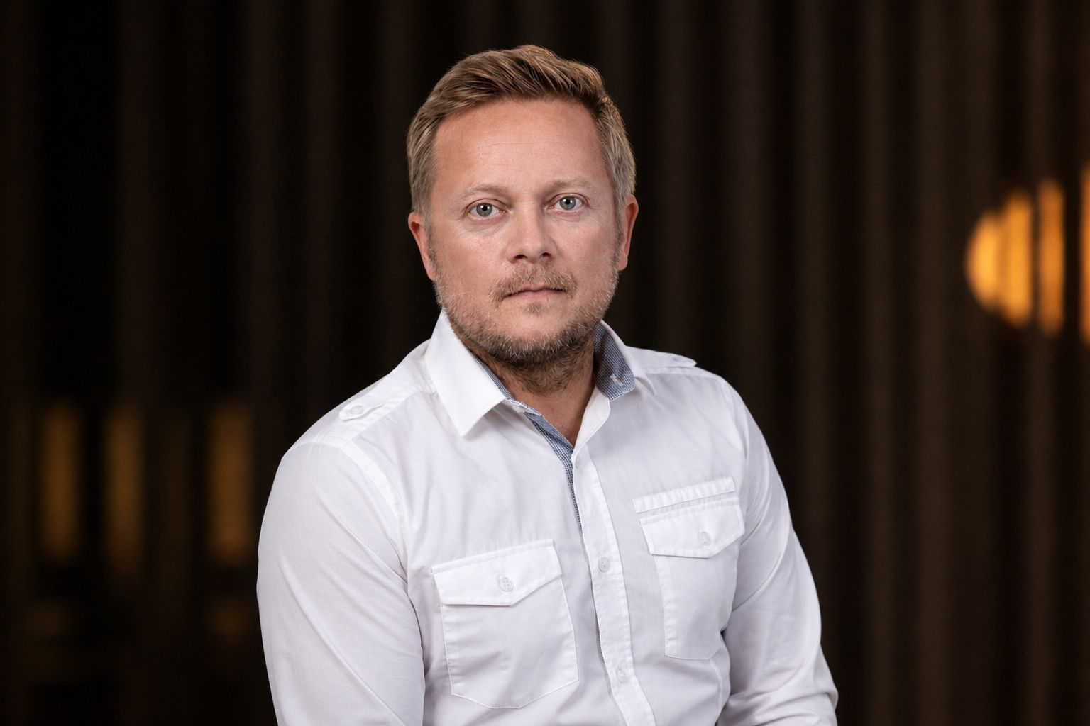 Portrait of a man in a white shirt against a dark, softly lit background