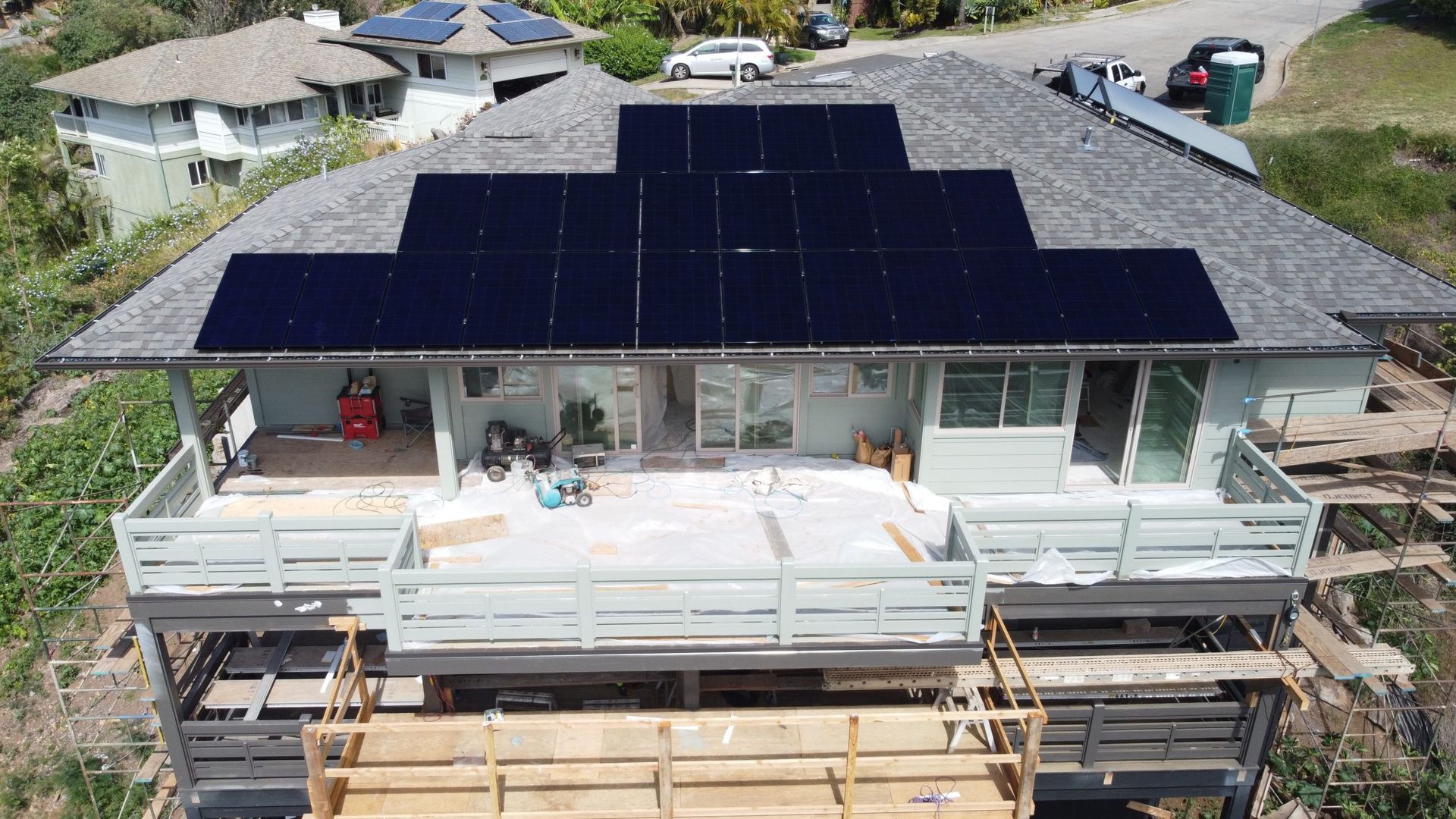 House with rooftop solar panels and a front balcony under construction, viewed from above.