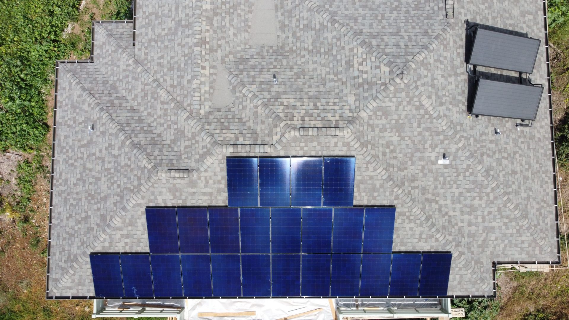 Rooftop with blue solar panels installed along the lower edge on gray shingles.