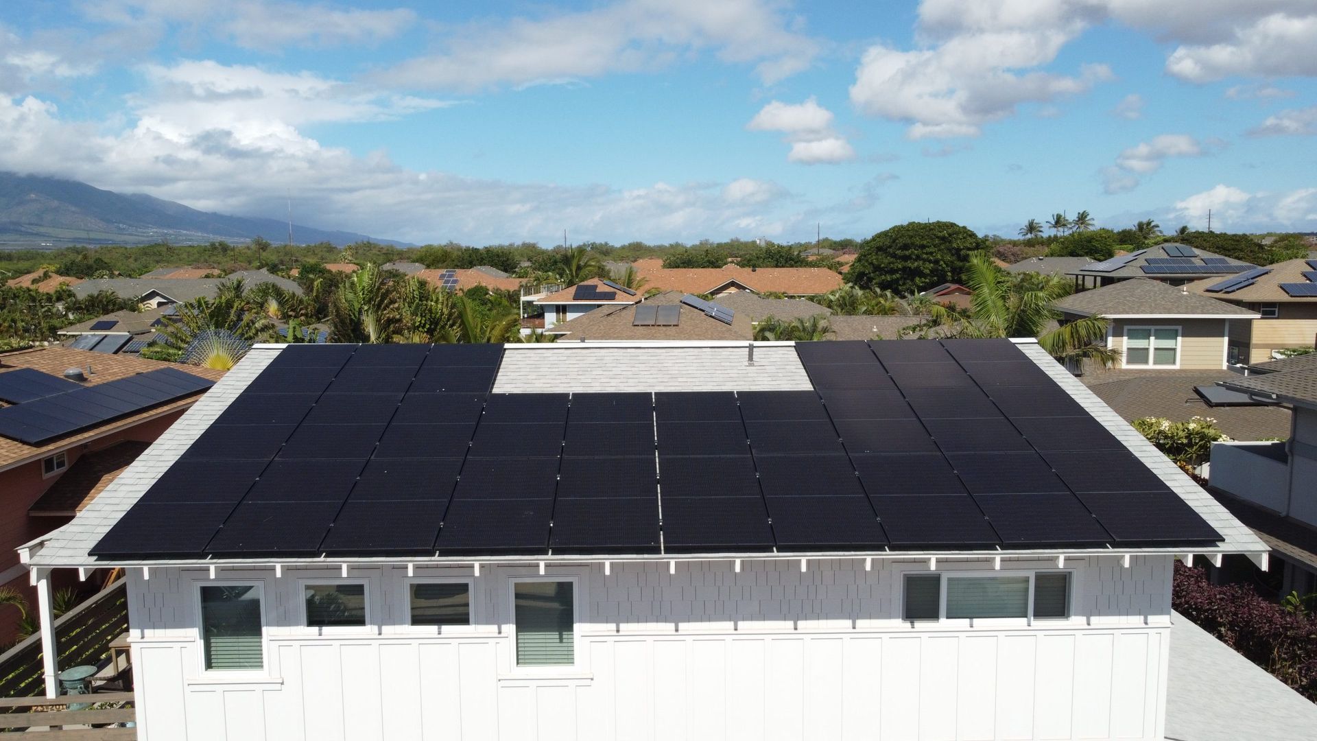 House rooftop covered with black solar panels under a clear sky, with mountains in the distance
