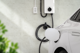 White electric car charging beside a wall-mounted charger in a garage